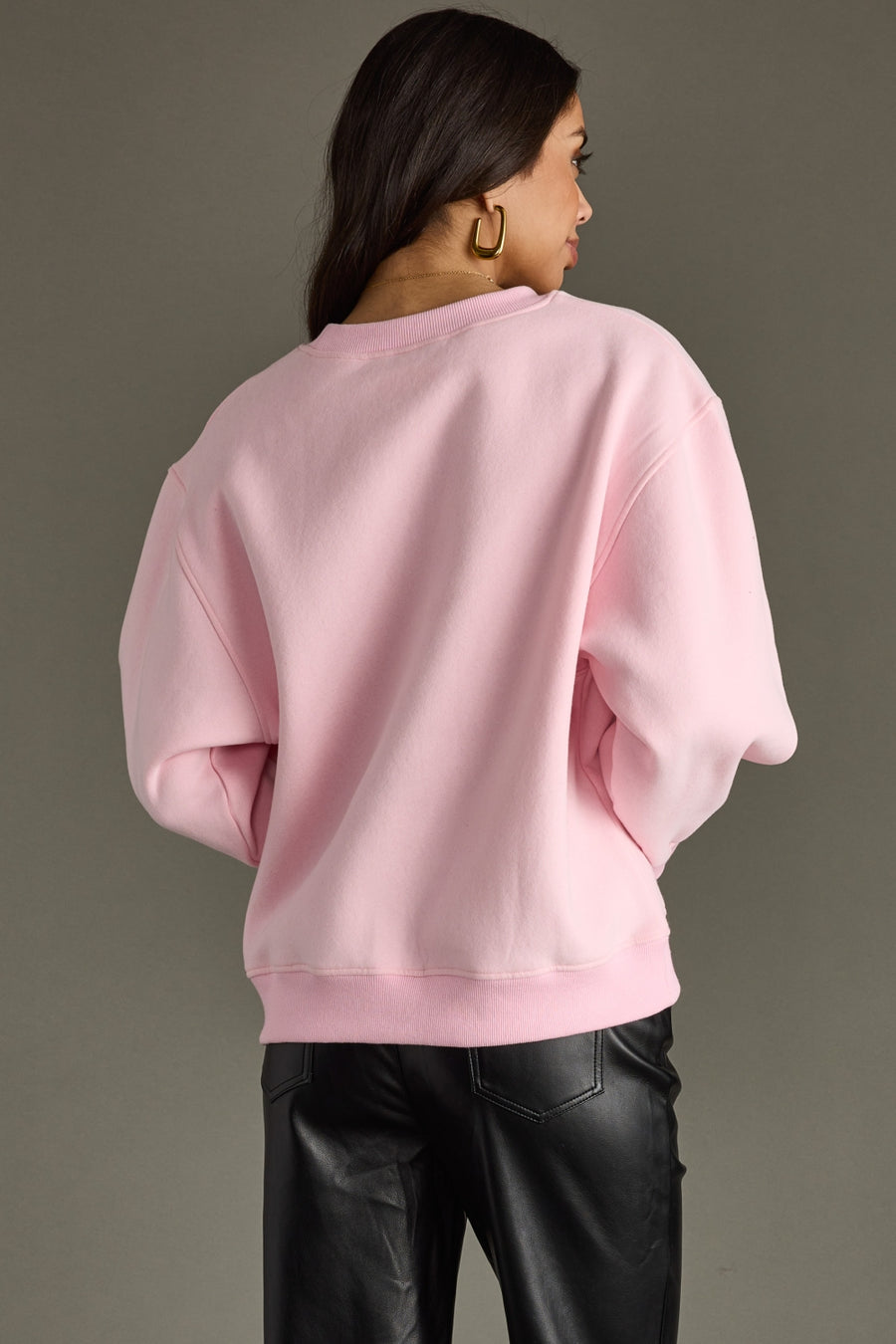 Person wearing a pink sweatshirt and black pants against a gray background