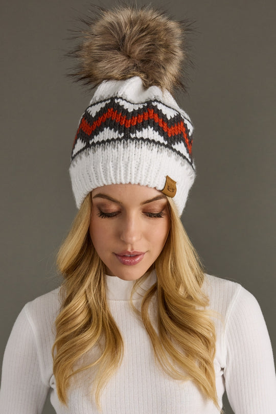 Woman wearing a white knit beanie with a brown pom-pom against a gray background