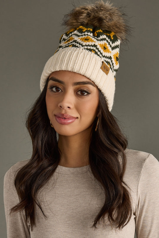 Woman wearing a patterned knit beanie with a fur pom-pom against a gray background
