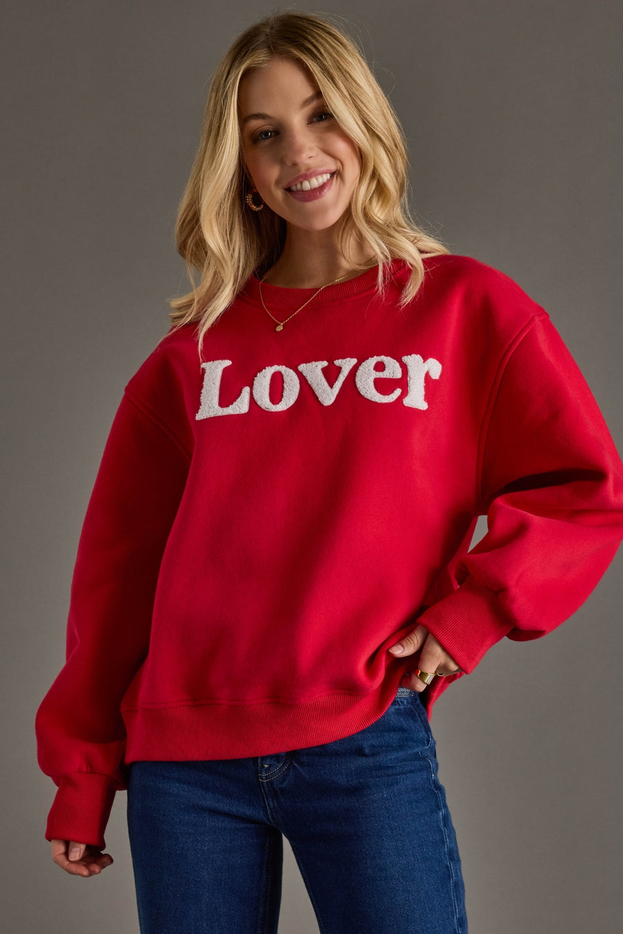 Woman wearing a red sweatshirt with 'Lover' printed on it against a gray background
