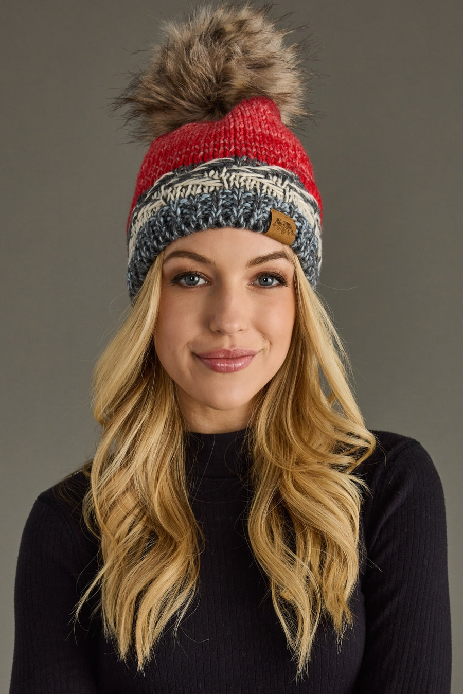 Woman wearing a red and gray striped beanie with a pom-pom on a gray background