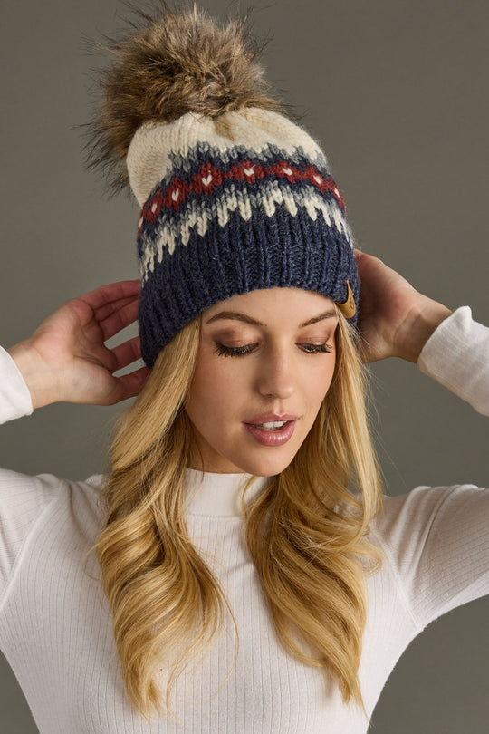 Woman wearing a colorful knit beanie with a pom-pom against a neutral background