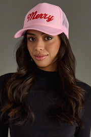 Woman wearing a pink trucker hat with 'Merry' text on a gray background