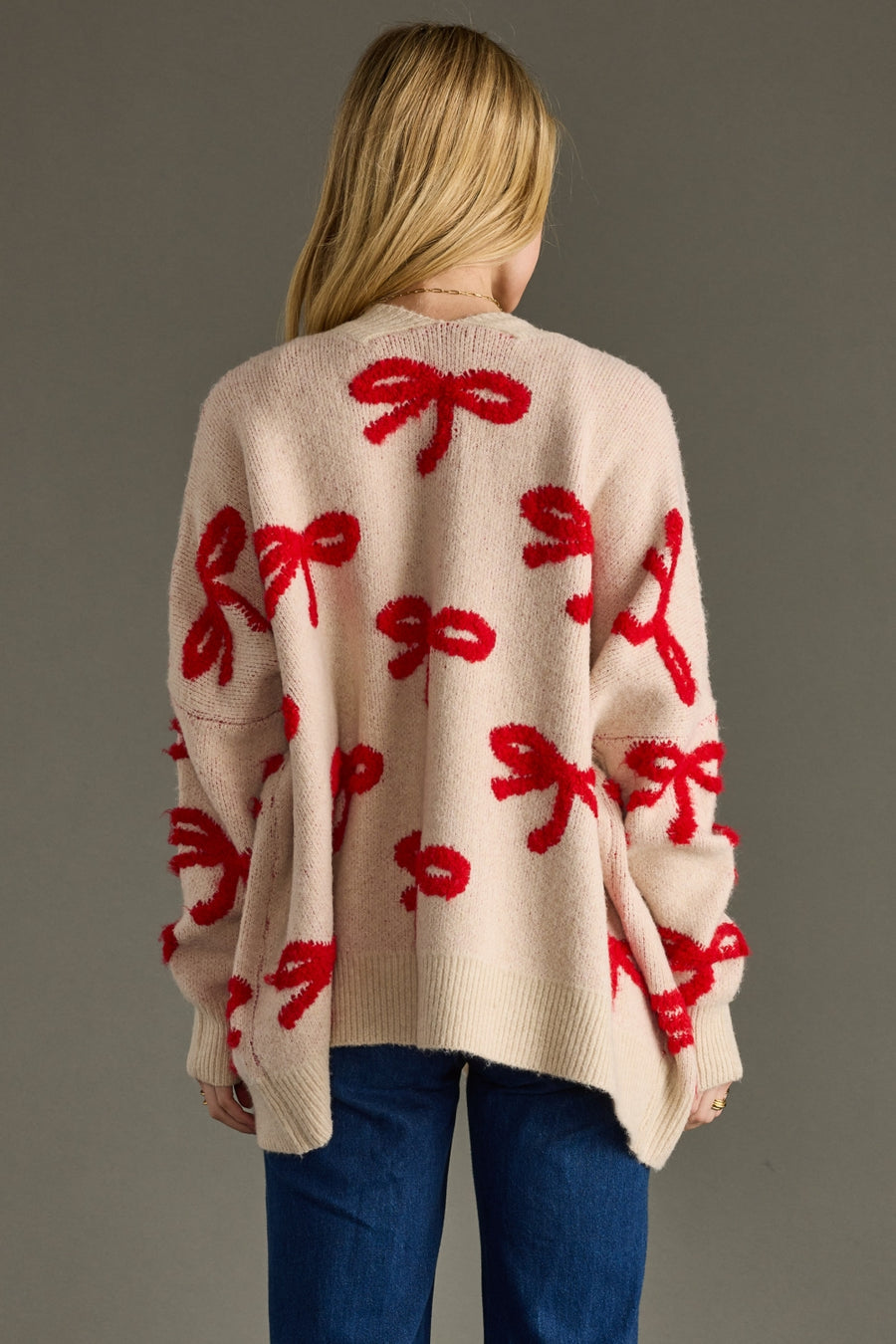 Beige sweater with red bow patterns worn by a person on a gray background