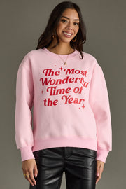 A woman smiles against a gray background wearing a pink oversized Panache Apparel Collection "The Most Wonderful Time Of The Year Sweatshirt" with black leather pants.