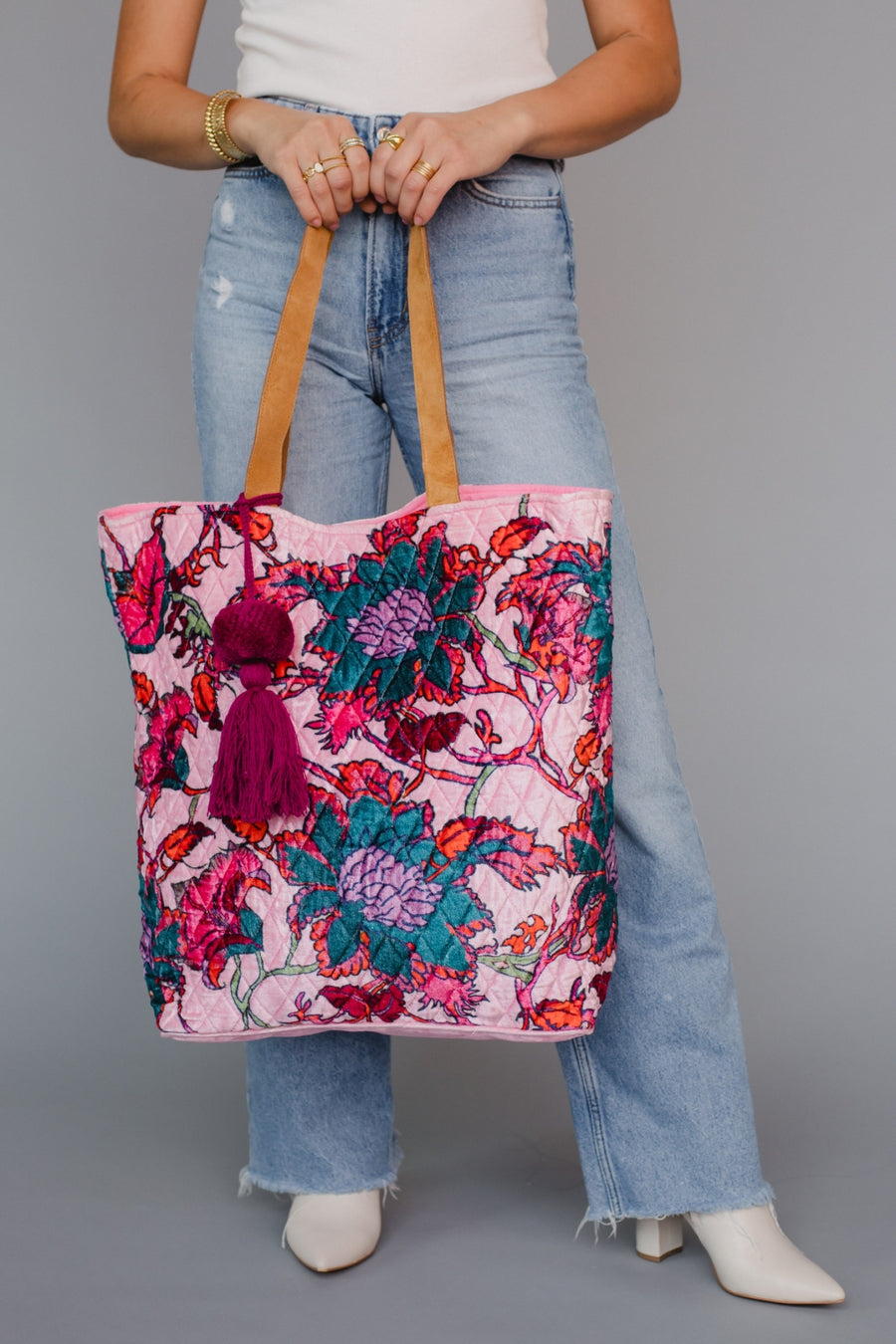 Person holding a colorful floral tote bag against a gray background