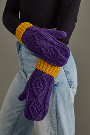 Purple mittens with yellow cuffs worn by a person against a neutral background