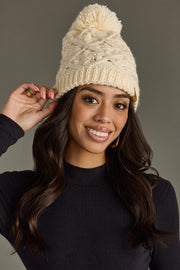 Woman wearing a cream knit beanie with a pom-pom against a gray background