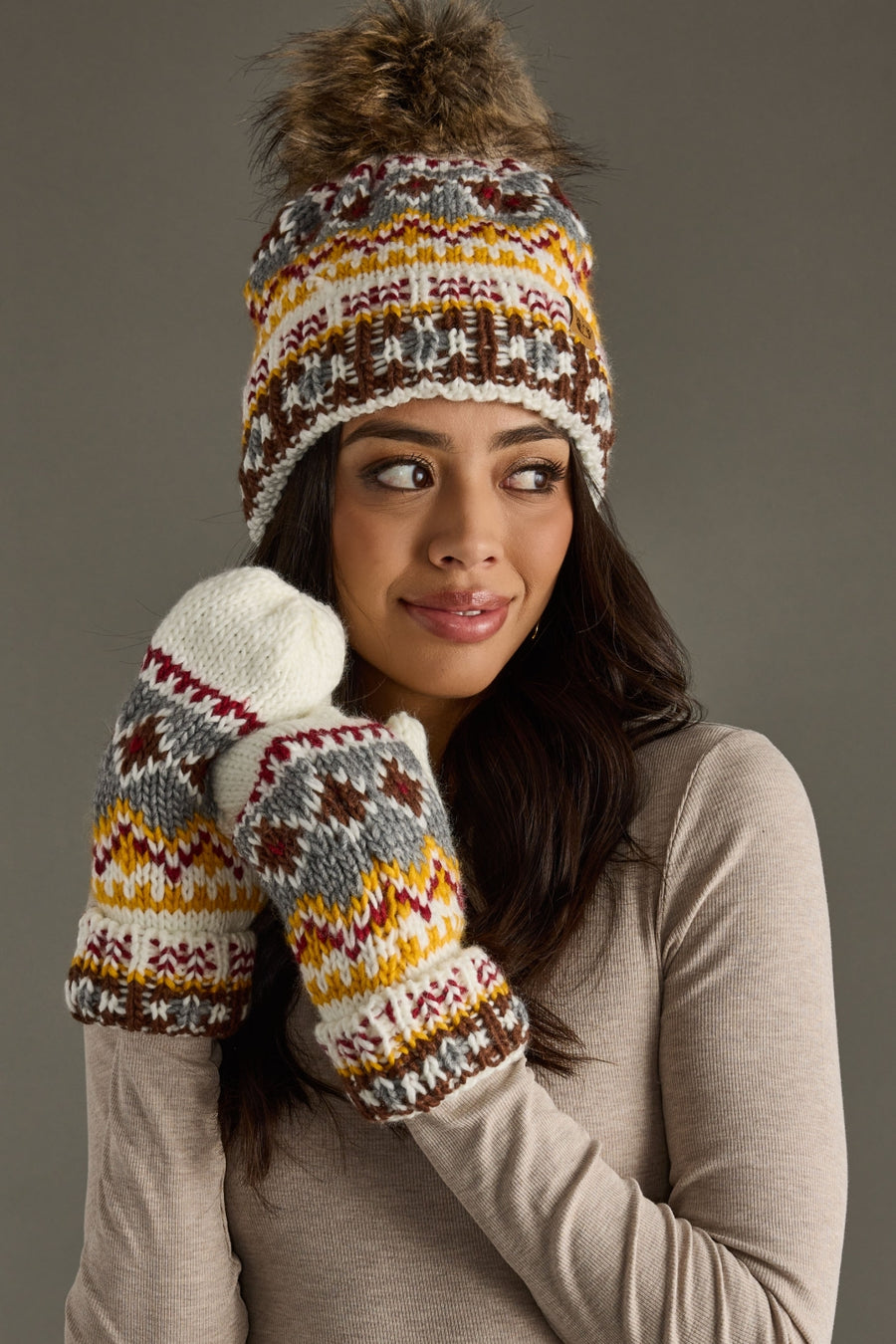 Woman wearing a patterned knit hat and mittens against a gray background