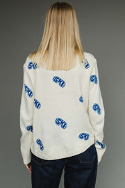 Person wearing a white sweater with blue and red patterns on a gray background