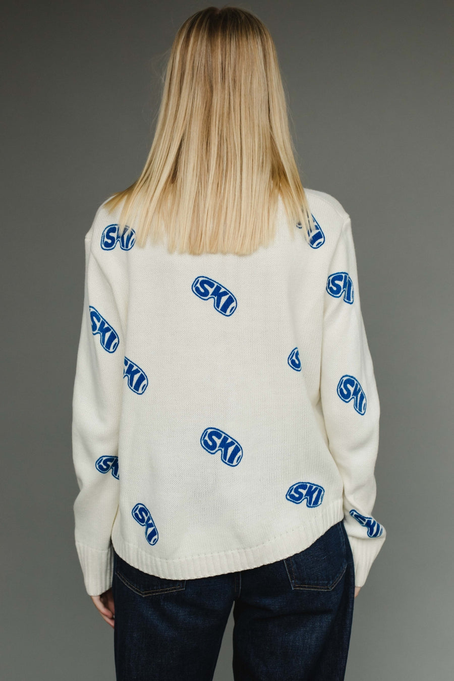 Person wearing a white sweater with blue and red patterns on a gray background