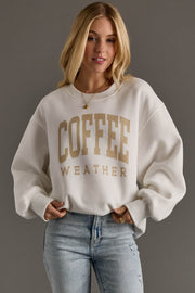 Woman wearing a beige sweatshirt with 'COFFEE WEATHER' text on a gray background