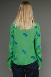 Person wearing a green sweater with blue patterns on a gray background
