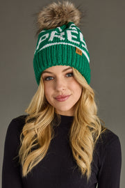 Woman wearing a green beanie with a fur pom-pom against a gray background