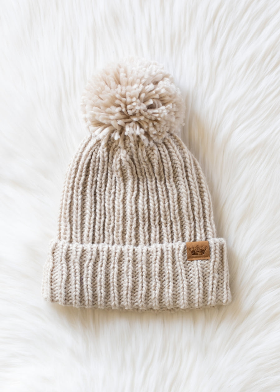 Beige knit beanie with pom-pom on a white textured background