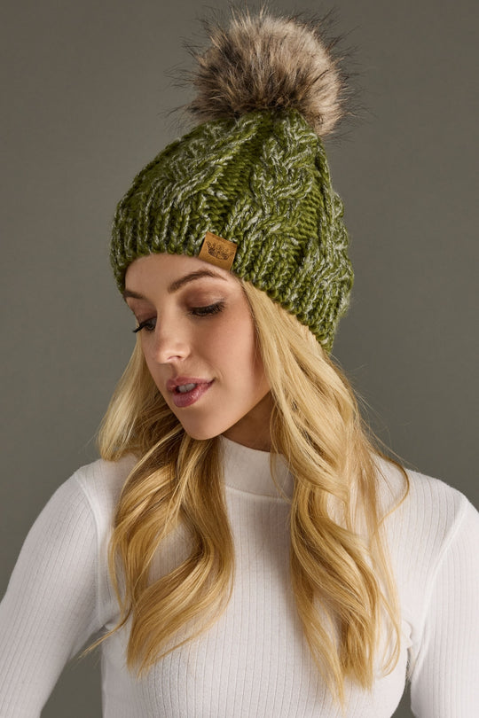 Woman wearing a green knit beanie with a fur pom-pom on a gray background