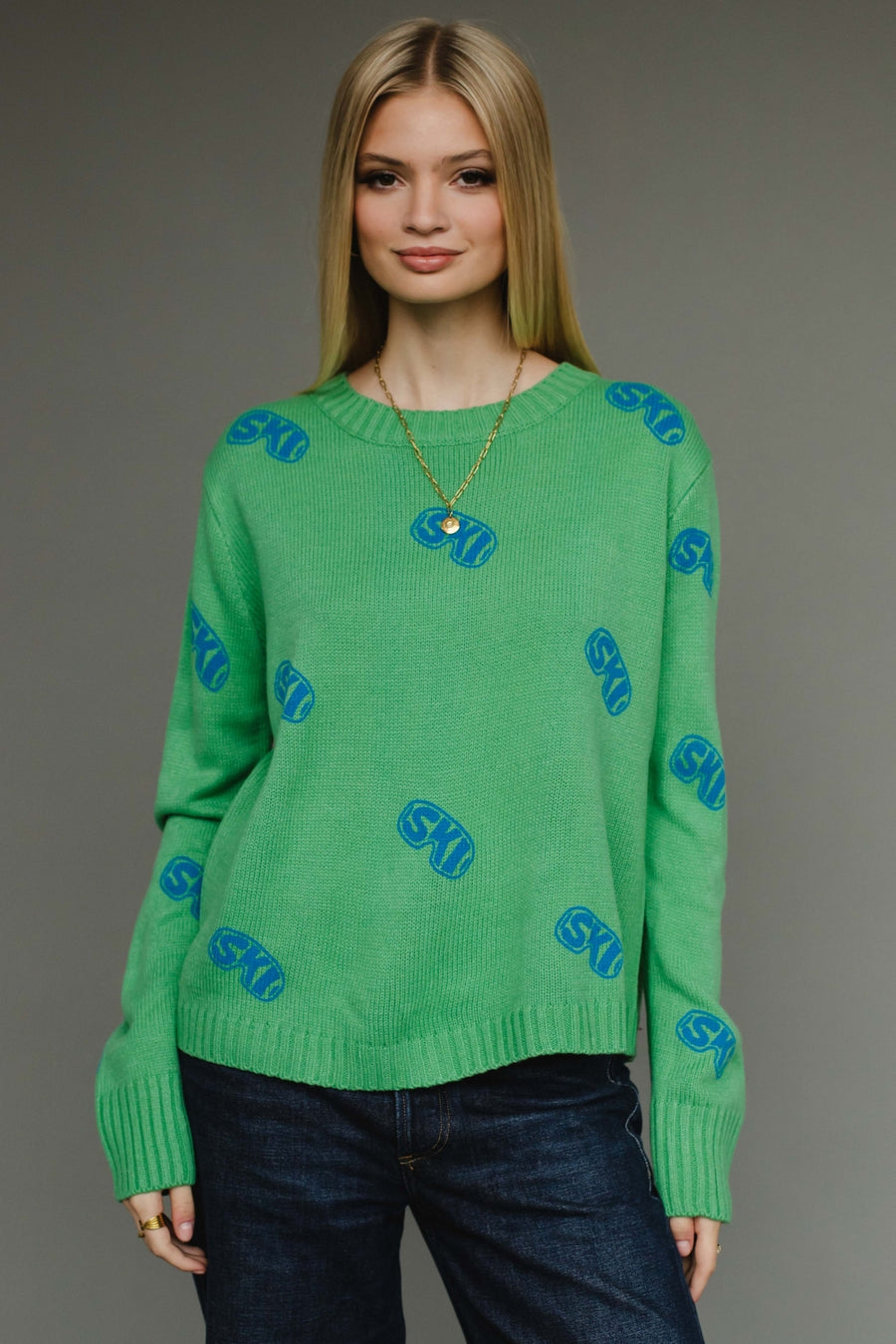 Woman wearing a green sweater with blue patterns on a gray background