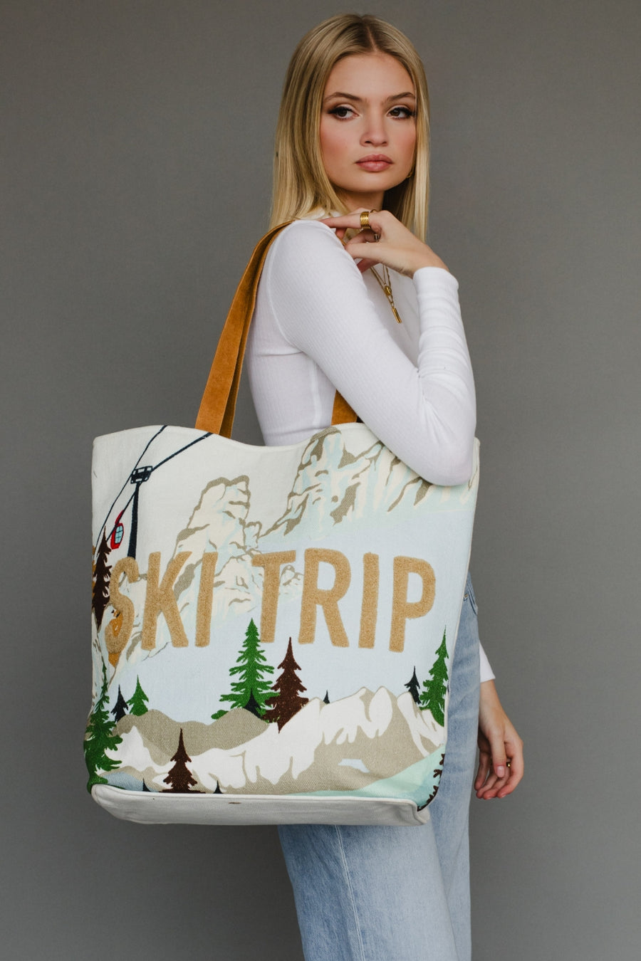 Woman holding a tote bag with 'Ski Trip' and mountain design against a gray background