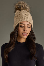 Woman wearing a beige knit beanie with a pom-pom on a gray background