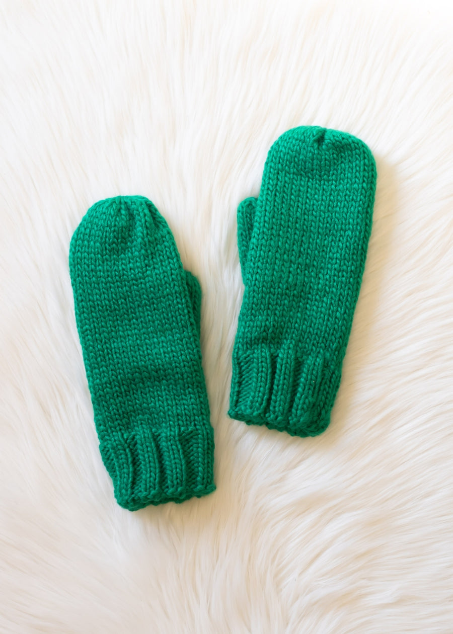 Pair of green knitted mittens on a white fur surface