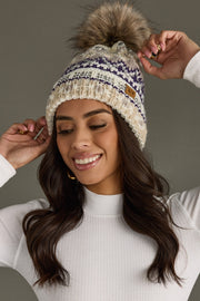 Woman wearing a knit beanie with a pom-pom against a neutral background
