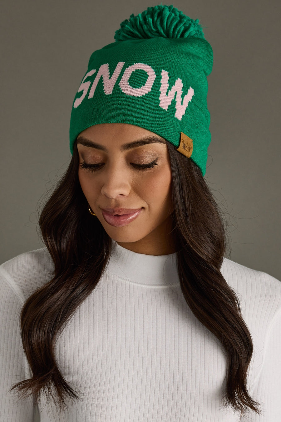 Woman wearing a green beanie with 'SNOW' text on a gray background