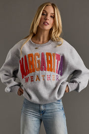 Woman wearing a gray sweatshirt with colorful text 'MARGARITA WEATHER' against a plain background