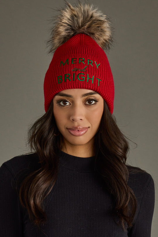 Person wearing a red beanie with a fur pom-pom and 'Merry and Bright' text on a gray background