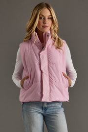 Woman wearing a pink puffer vest over a white shirt with a gray background