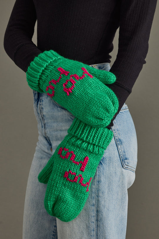 Green mittens with pink text worn by a person against a neutral background
