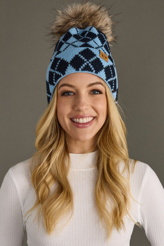 Woman wearing a blue patterned beanie with a fur pom-pom against a gray background