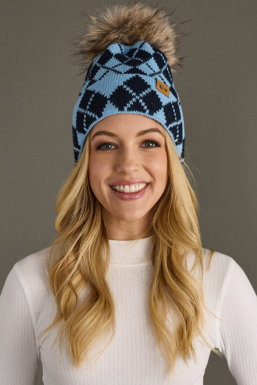 Woman wearing a blue patterned beanie with a fur pom-pom against a gray background