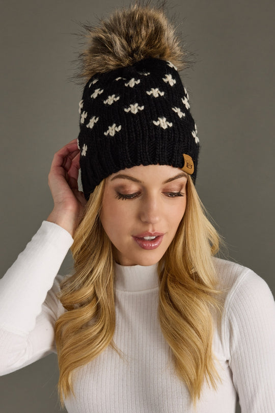 Woman wearing a black knit beanie with a fur pom-pom on a gray background