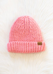 Pink knit beanie with a brown label on a white fur background