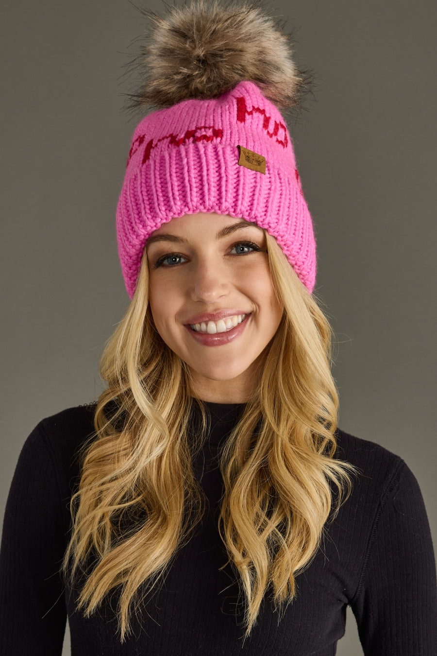 Person wearing a pink knit beanie with a fur pom-pom on a gray background