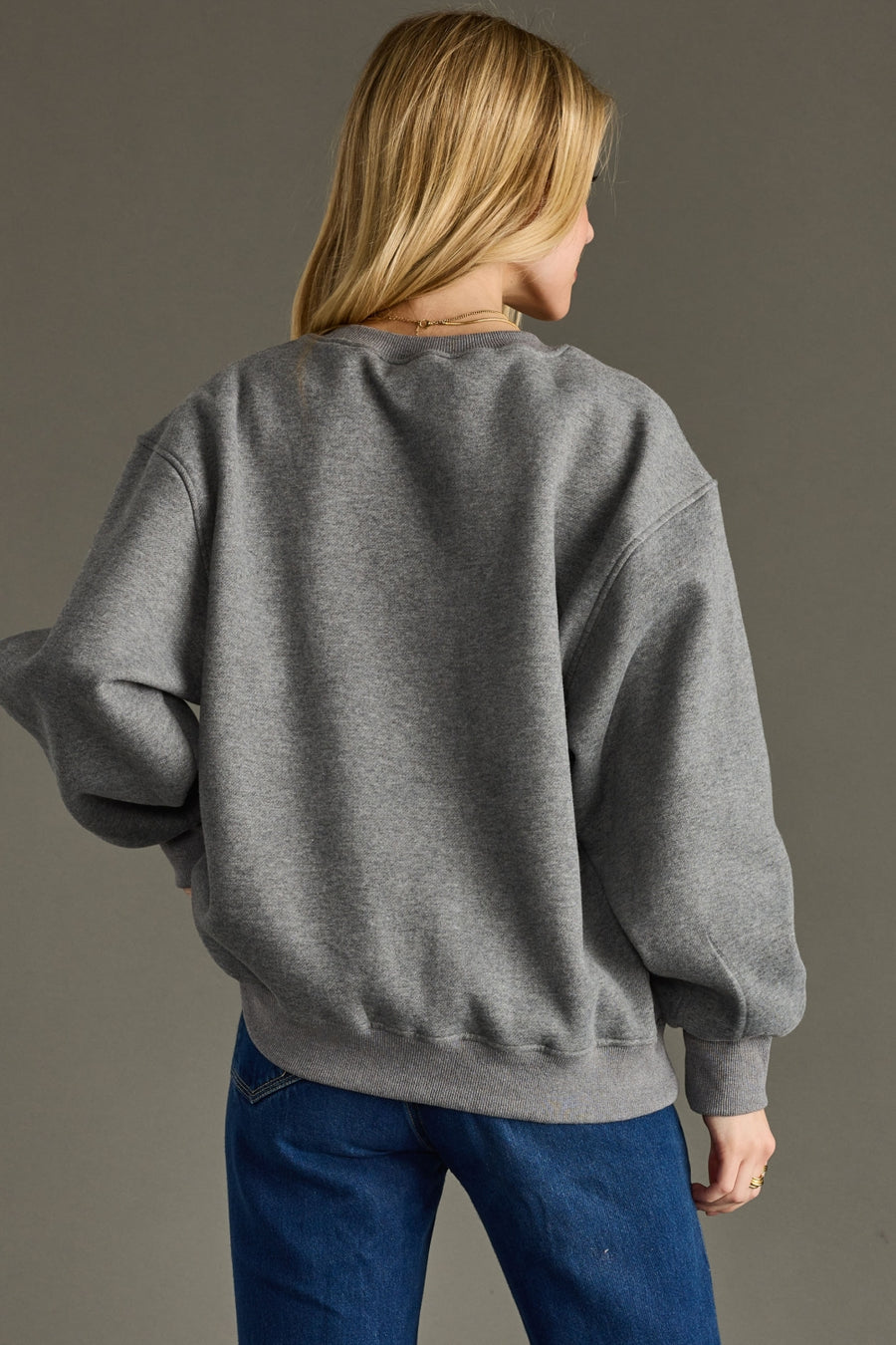 Person wearing a gray sweater and blue pants against a gray background
