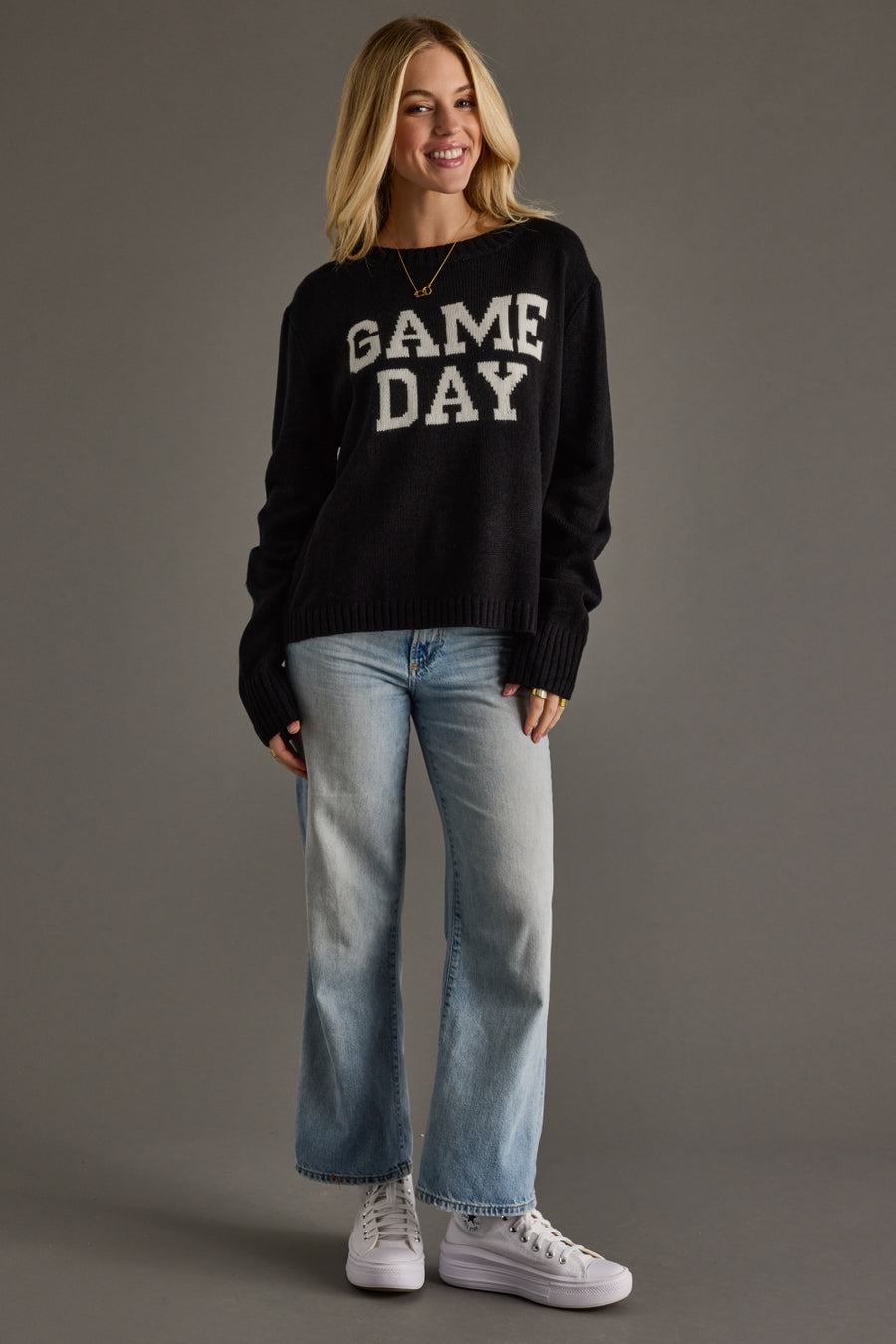 Woman wearing a black 'GAME DAY' sweater with blue jeans on a gray background