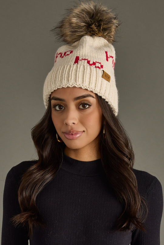 Woman wearing a cream knit beanie with a pom-pom on a gray background