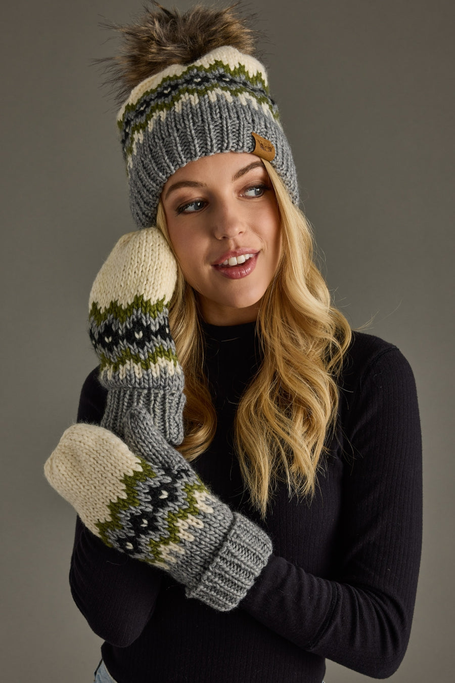 Woman wearing a gray knit hat and mittens with a pom-pom on a gray background