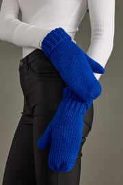 Person wearing blue knitted mittens with a plain background