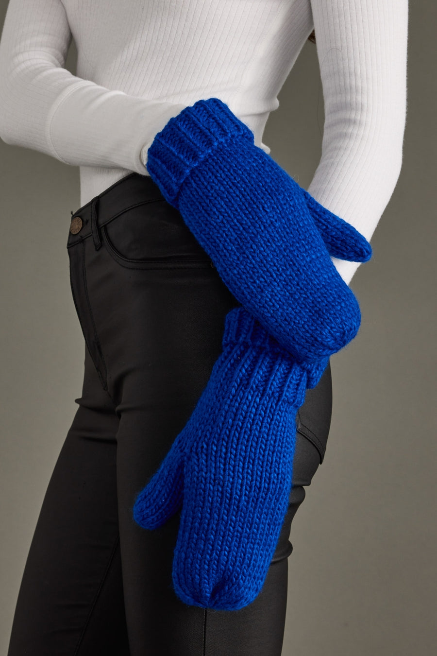 Person wearing blue knitted mittens with a plain background