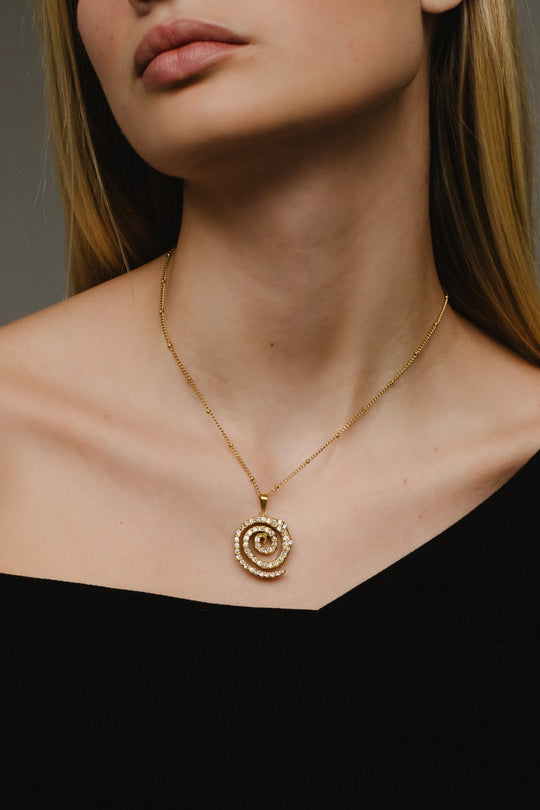 Close-up of a person wearing a gold spiral pendant necklace against a neutral background
