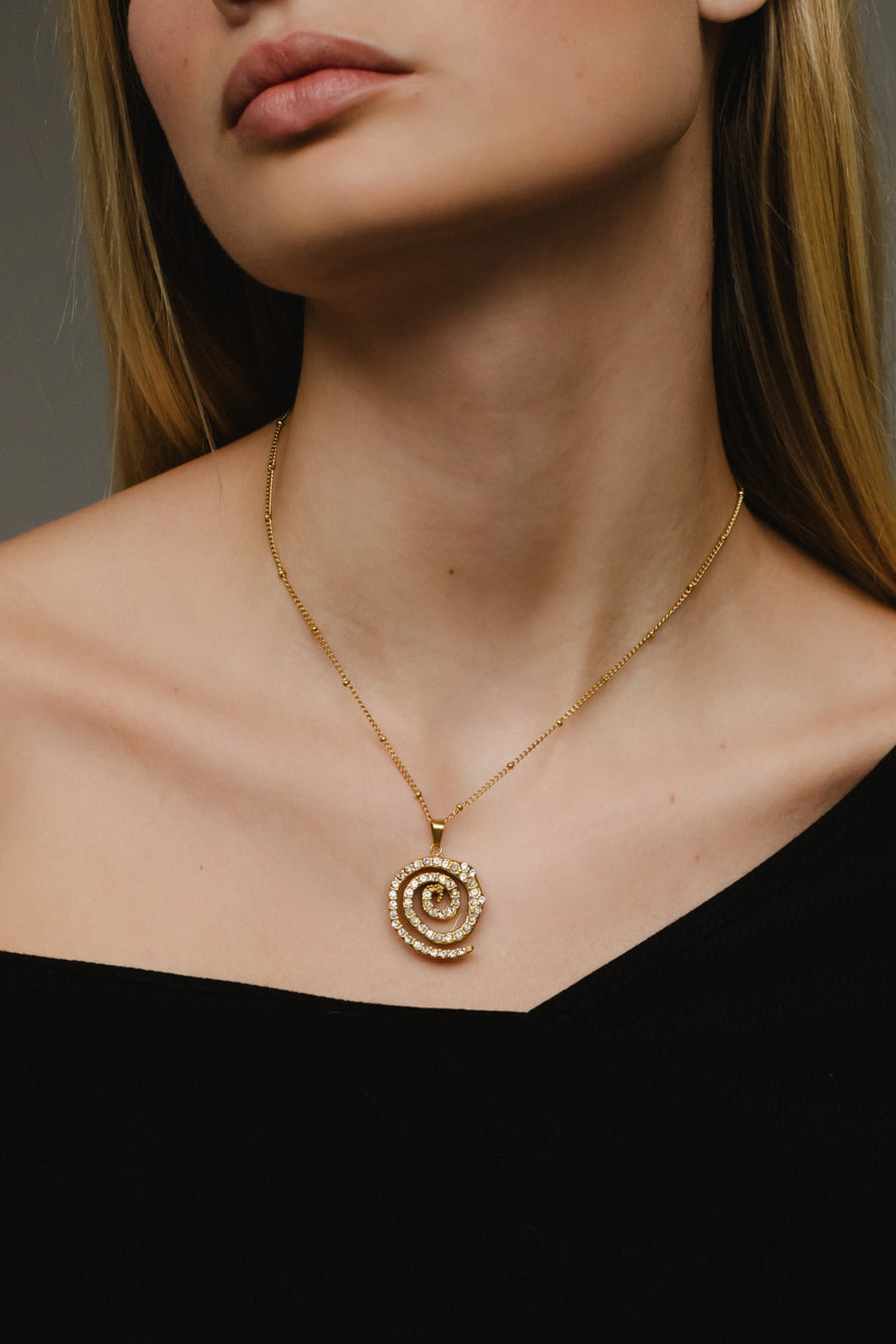 Close-up of a person wearing a gold spiral pendant necklace against a neutral background