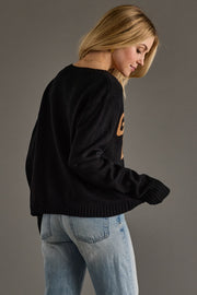 Woman wearing a black sweater and light blue jeans against a gray background
