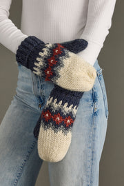 Knit mittens with a pattern held by a person wearing jeans and a white long-sleeve shirt.