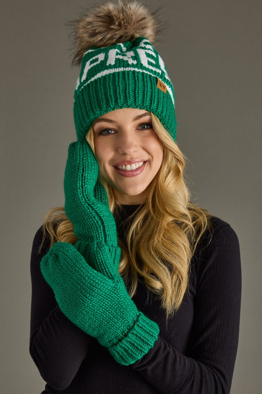 Woman wearing a green knit hat and gloves with a brand logo on a gray background