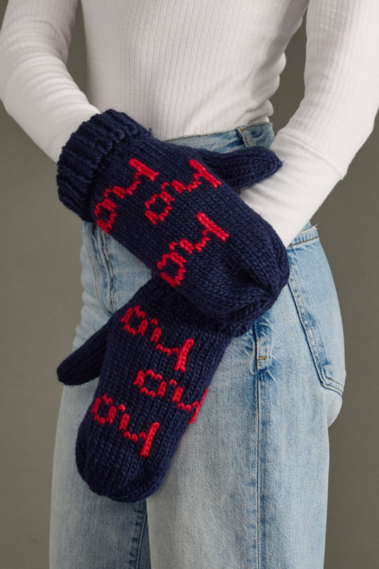 Navy blue mittens with red text worn by a person against a neutral background