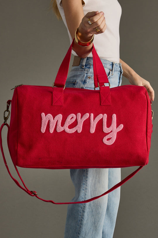 Red bag with 'merry' text held by a person against a gray background