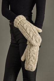 Person wearing beige knitted mittens against a gray background