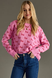 Woman wearing a pink sweater with 'ho ho ho' pattern and blue jeans on a gray background